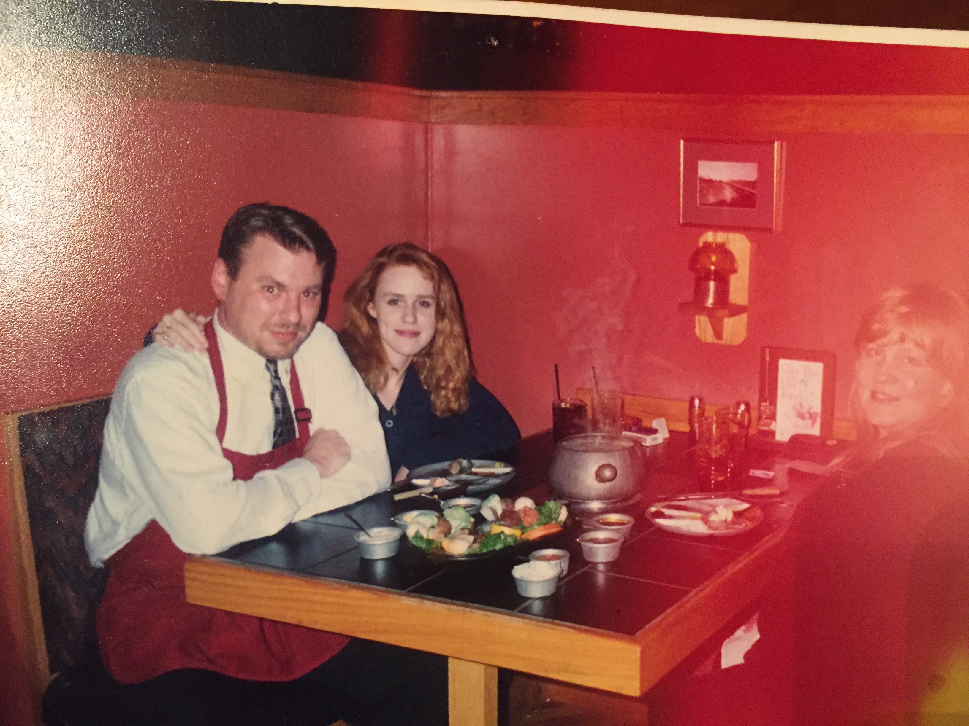 Two women and a man sitting at a booth in a restaurant. The right side of the photos' lighting is blown out by what appears to be a camera flash, tinging the photo red.